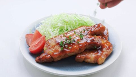 Sprinkling chopped green onions on a plate of Japanese ginger pork.