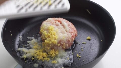 Grating onion and ginger into a pan with ground chicken to make the ramen base.