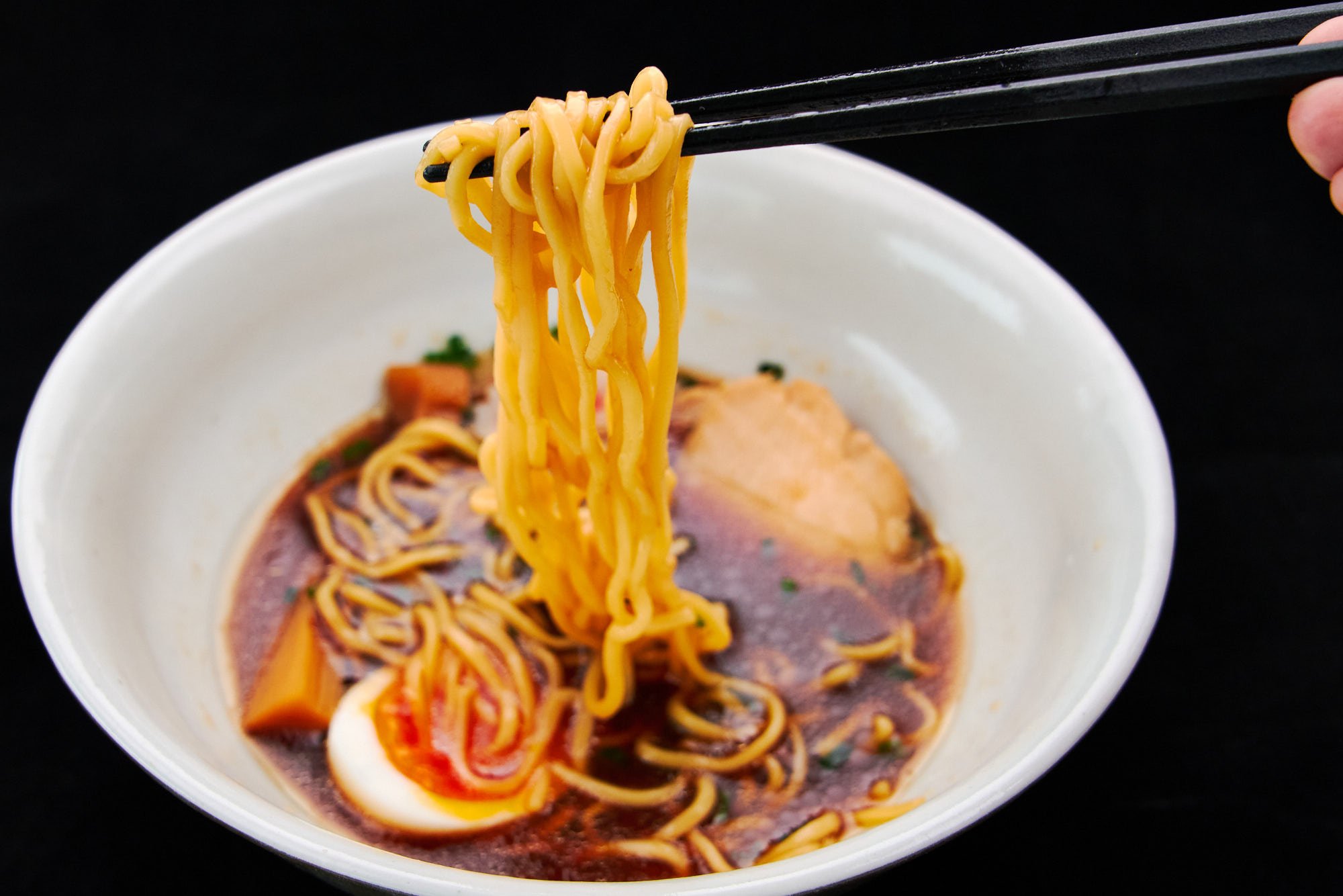 A steaming bowl of shoyu ramen topped with chicken chashu and narutomaki, with noodles lifted mid-scoop for the perfect bite.