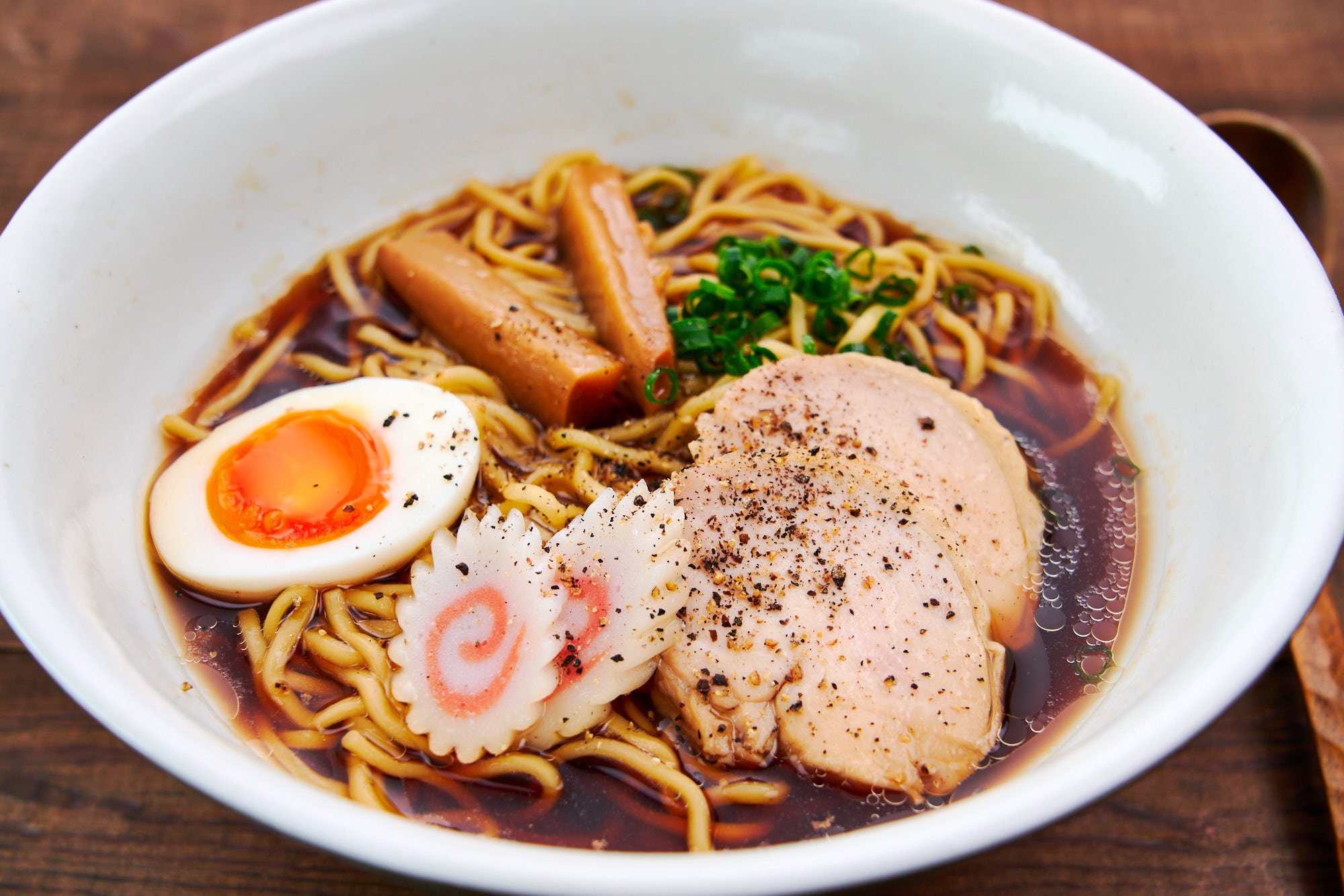 A hearty bowl of shoyu chicken ramen topped with ground black pepper, seasoned egg, menma, and scallions over a glossy soy sauce broth.
