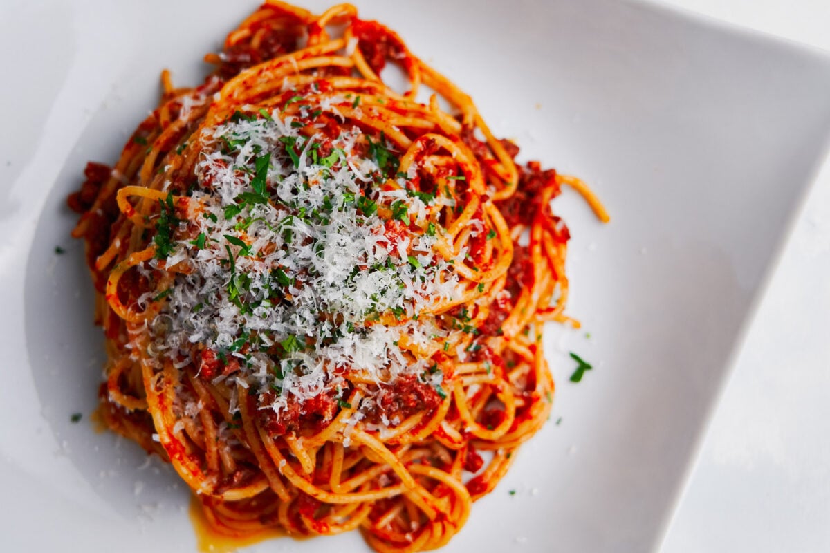 Overhead view of the best spaghetti from scratch on a white plate sprinkled with parmesan and parsley.