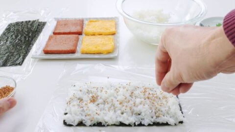 Sprinkling rice and nori with salt and toasted sesame seeds.