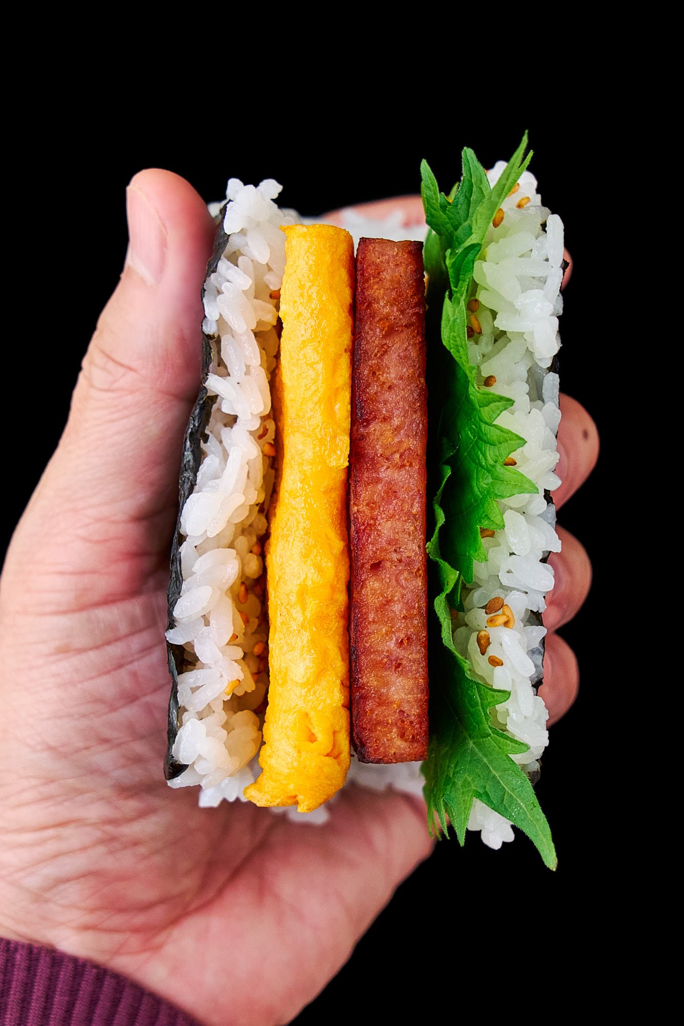 Hand held Spam Onigiri Sandwich with egg and green shiso leaves.