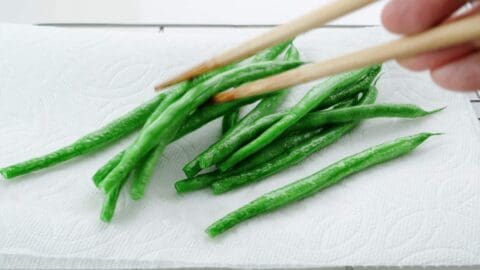 Flash fried green beans draining on a paper towel lined rack.