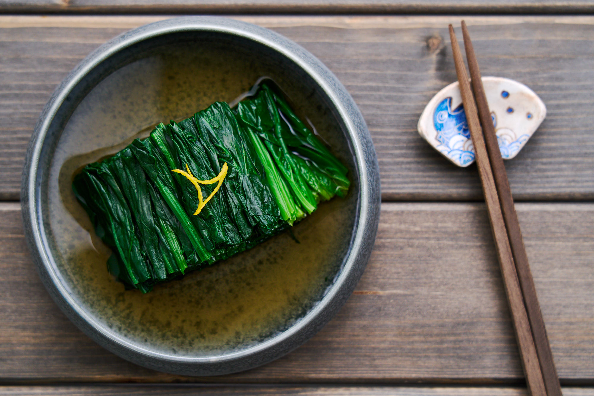 A bowl of Japanese spinach salad (Ohitashi) with dashi broth and yuzu peel.