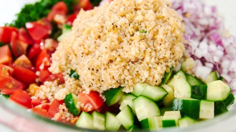 A glass bowl brims with neat quadrants of chopped parsley, juicy tomato, cool cucumber, minced red onion, and a generous mound of fluffy bulgur, poised to be tossed into vibrant tabbouleh.