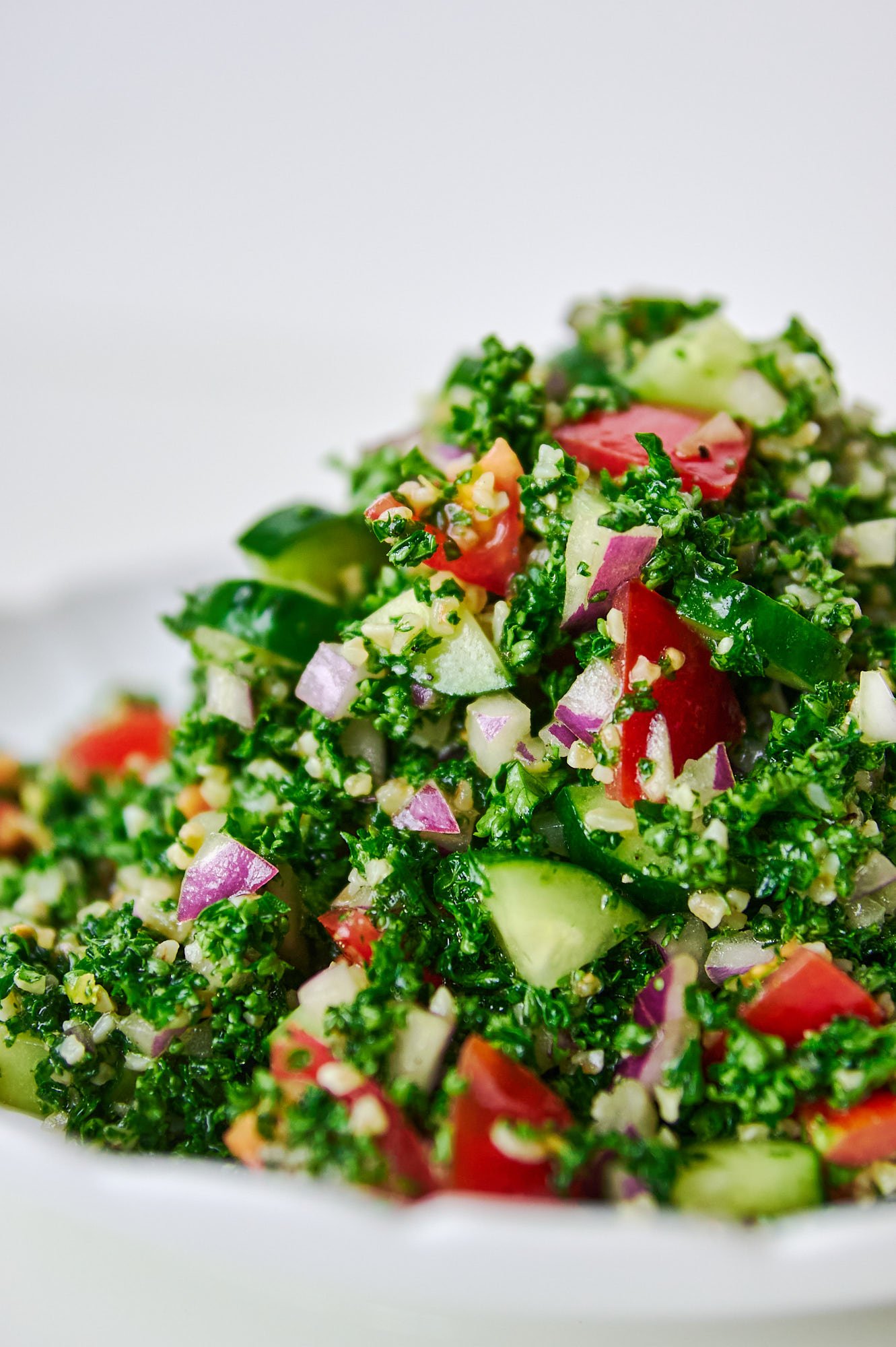 A towering mound of parsley-forward tabbouleh sits center-stage on a white dish, each jewel-toned tomato and cucumber piece catching the light.