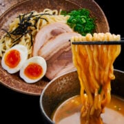 A bowl of creamy Tsukemen broth with noodles for dipping and a plate of accompaniments.