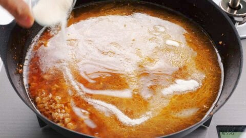 Adding chicken stock and gelatin to the ramen broth.