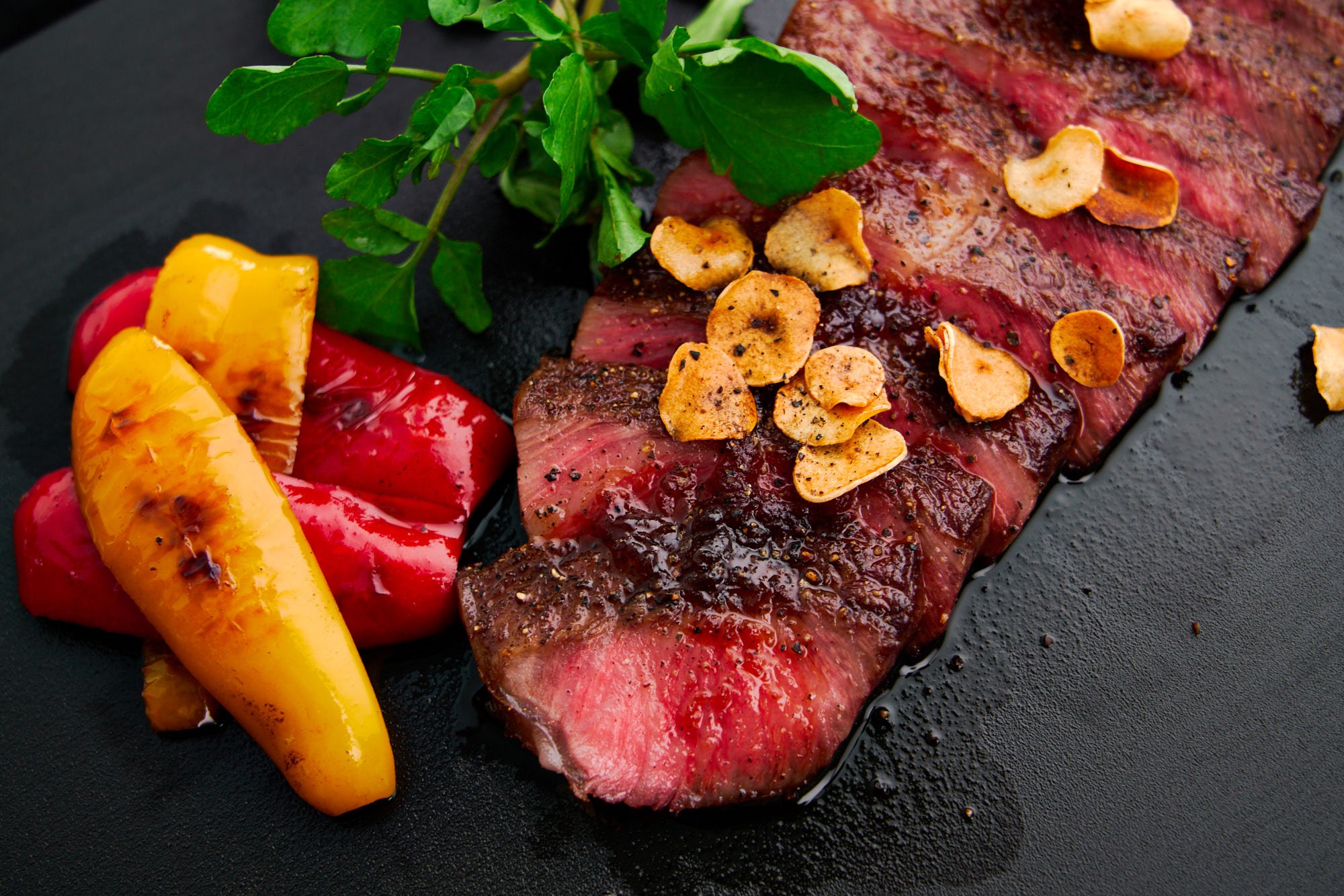 Closeup of a sliced A5 wagyu steak cooked to medium rare with a Japanese steak sauce and garlic chips.