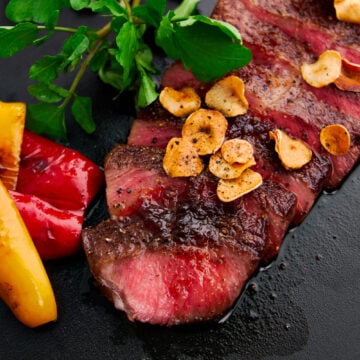 Closeup of a sliced A5 wagyu steak cooked to medium rare with a Japanese steak sauce and garlic chips.