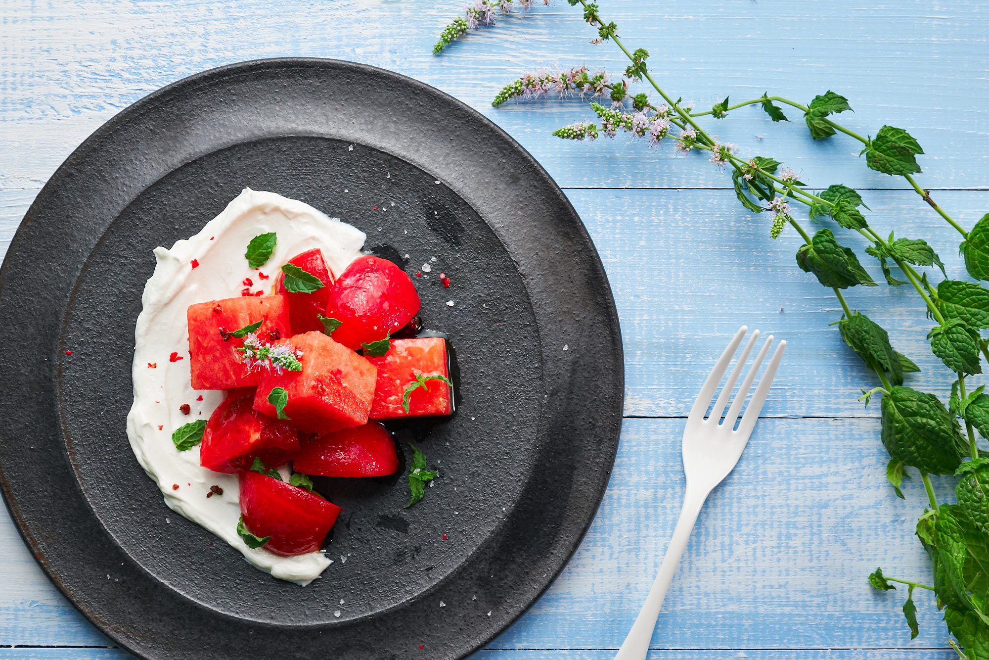 Summer watermelon and tomato salad on a bed of labneh with mint, and pink peppercorns.