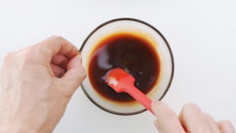 Mixing yakisoba sauce in a glass bowl with a spatula.