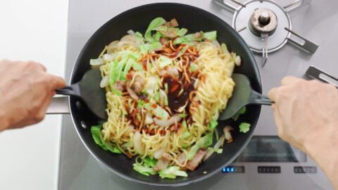 Ramen noodles and vegetables in a frying pan with yakisoba sauce.